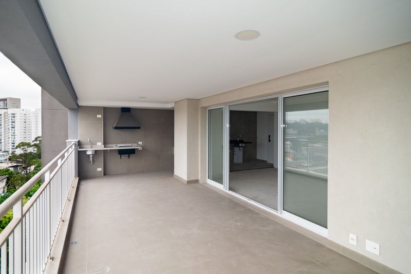 Varanda do apartamento, com churrasqueira e porta de vidro para a sala